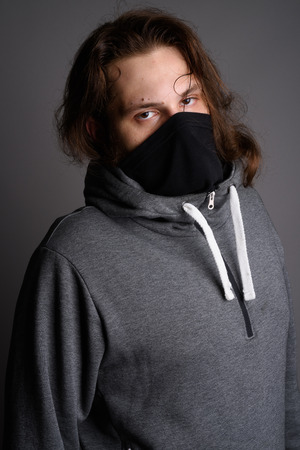 Young bearded man wearing gray hoodie and mask against gray backの写真素材