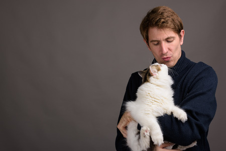 Handsome man holding cute cat against gray backgroundの写真素材
