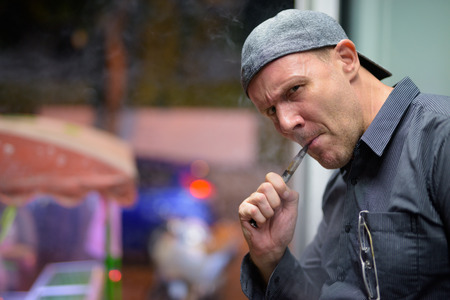 Mature man smoking electronic cigarette in the streets at night