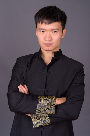 Studio shot of young Chinese man against gray backgroundの写真素材