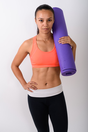 Studio shot of young Asian woman standing while holding yoga matの写真素材