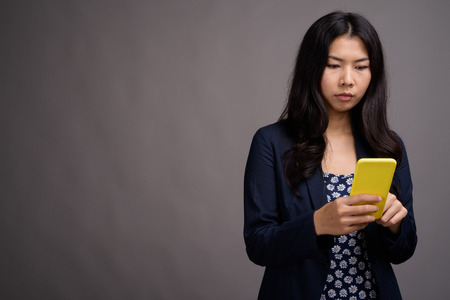 Asian woman using mobile phone against gray backgroundの写真素材