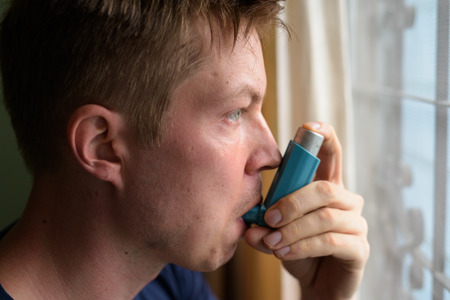 Young handsome man using asthma inhaler at homeの写真素材