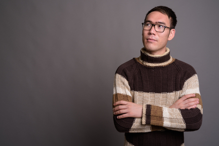 Young Asian man wearing turtleneck sweater against gray backgrouの写真素材