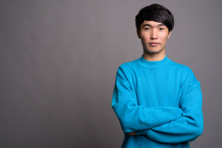 Young Asian man wearing blue sweater against gray backgroundの写真素材