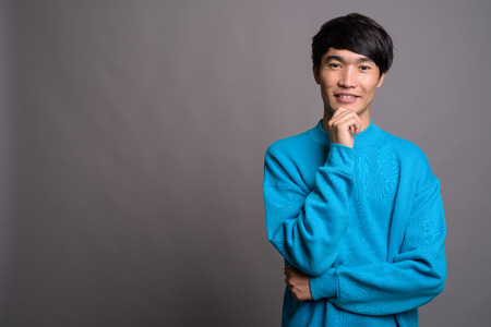 Young Asian man wearing blue sweater against gray backgroundの写真素材
