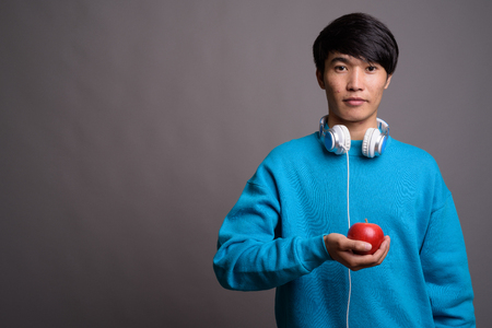 Young Asian man wearing headphones against gray backgroundの写真素材