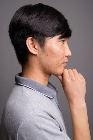 Young Asian man wearing gray polo shirt against gray backgroundの写真素材