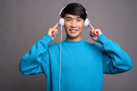 Young Asian man listening to music against gray backgroundの写真素材