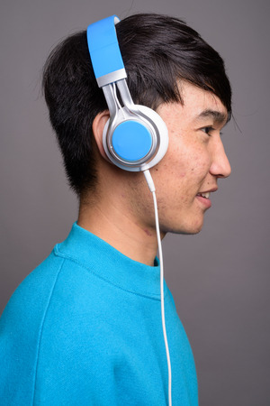 Young Asian man listening to music against gray backgroundの写真素材
