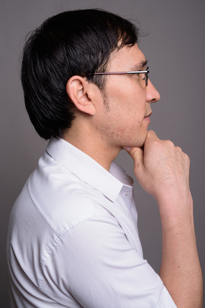 Young Asian nerd man wearing eyeglasses against gray backgroundの写真素材