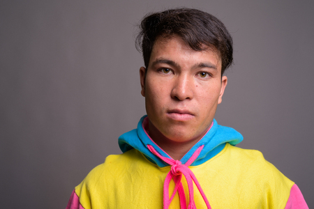 Young Asian man wearing colorful hoodie against gray backgroundの写真素材