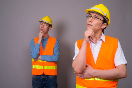Two young Asian men construction worker together against gray baの写真素材