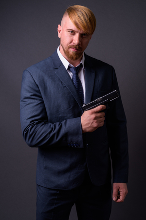 Bearded businessman with handgun against gray backgroundの写真素材