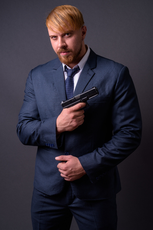 Bearded businessman with handgun against gray backgroundの写真素材