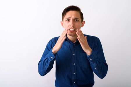 Studio shot of stressed young man looking shocked against white