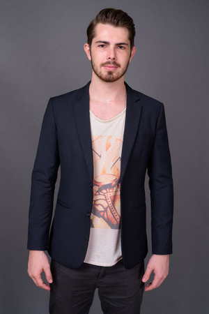 Young handsome bearded businessman against gray backgroundの写真素材