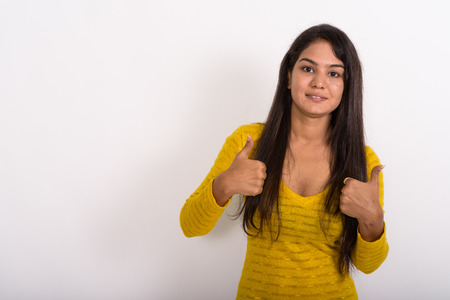 Studio shot of young happy Indian woman smiling while giving thuの写真素材