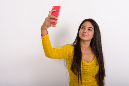 Studio shot of young happy Indian woman smiling while taking selの写真素材