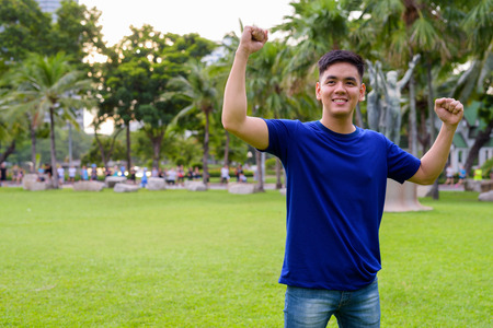 Young handsome Asian man relaxing at the park with arms raisedの写真素材