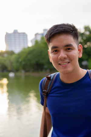 Young handsome Asian tourist man with backpack relaxing at the pの写真素材