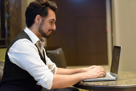 Profile view of young handsome Indian man using laptop in the loの写真素材