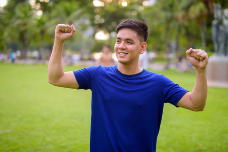 Young handsome Asian man relaxing at the park with arms raisedの写真素材