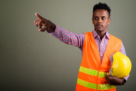 Young handsome African man construction worker against colored b