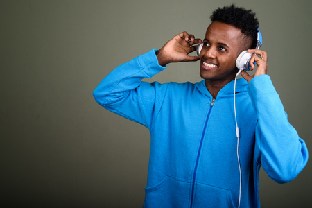 Young handsome African man listening to music against colored baの写真素材