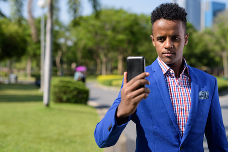 Young handsome African businessman using mobile phone at the parの写真素材