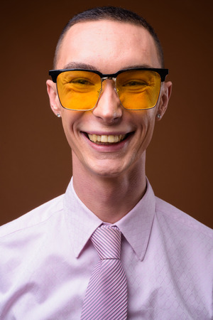 Young handsome androgynous businessman against brown backgroundの写真素材