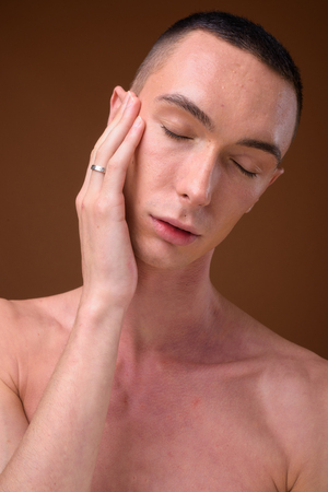 Young handsome androgynous man shirtless against brown backgrounの写真素材