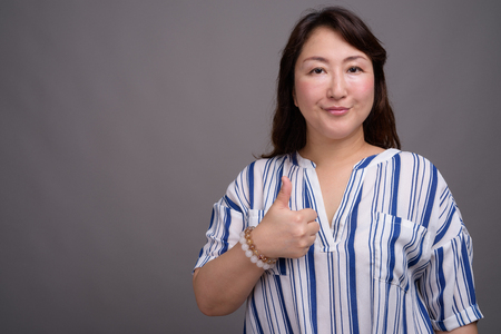 Mature beautiful Asian businesswoman against gray backgroundの写真素材