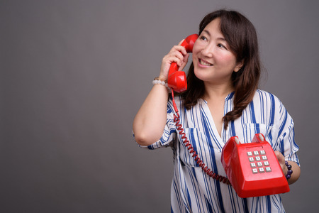 Mature beautiful Asian businesswoman holding old red phone