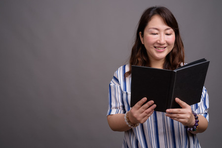 Portrait of mature beautiful Asian businesswoman reading book