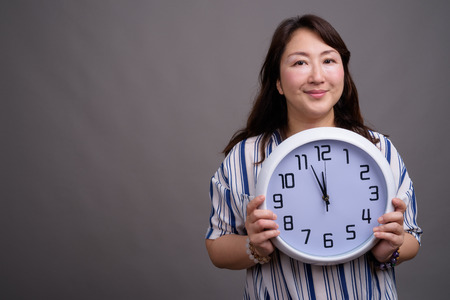 Portrait of mature beautiful Asian businesswoman holding clock