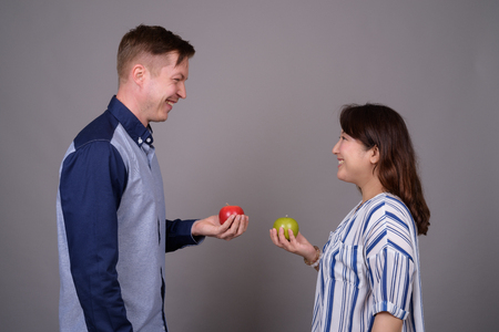 Multi ethnic diverse couple in studio holding green and red apple fruitの写真素材