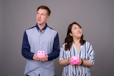 Portrait of couple holding piggy bank in hand while thinking