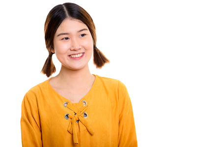 Studio shot of young happy Asian woman smiling while thinkingの写真素材