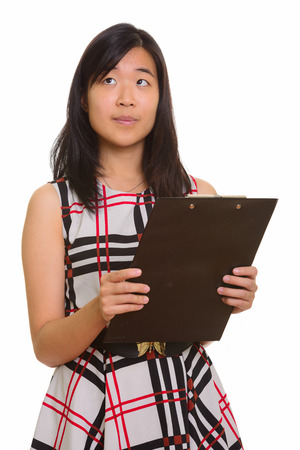Young beautiful Asian businesswoman holding clipboard while thinの写真素材