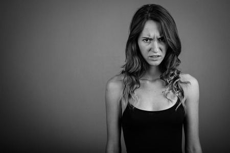 Young beautiful woman looking angry against gray background in bの写真素材