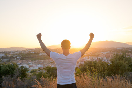 Rear View Of Happy Young Tourist Man Raising Arms On Top Of The Hillの写真素材