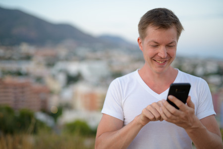 Young Happy Tourist Man Smiling While Using Phone In Nature