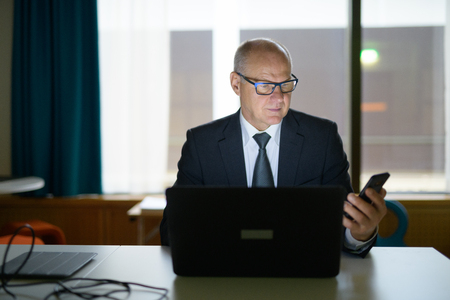 Senior Businessman Using Phone And Laptop At Work In The Officeの写真素材