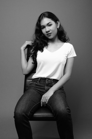 Young beautiful Asian woman sitting studio shot in black and whiteの写真素材
