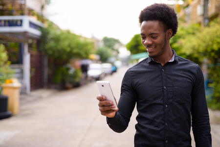 Young handsome African man using mobile phone outdoorsの写真素材