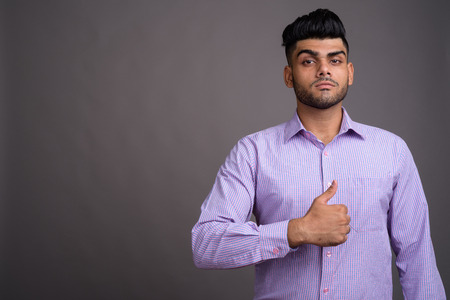 Young handsome Indian businessman against gray backgroundの写真素材