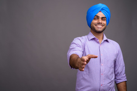 Young handsome Indian businessman wearing turban against gray baの写真素材
