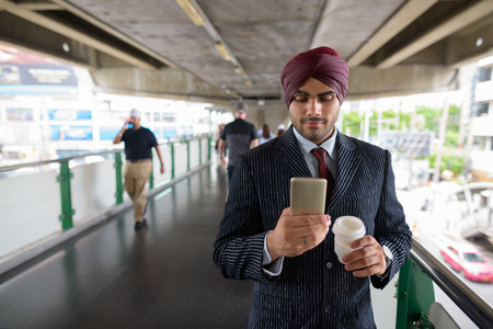 Indian businessman using mobile phone and holding coffee cup in cityの写真素材