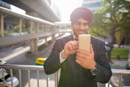 Indian businessman outdoors in city using phone with lens flareの写真素材